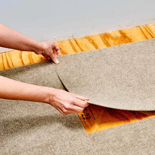 Installing beige carpet tiles on a plywood subfloor.