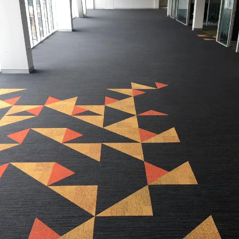 Modern black commercial carpet with orange and gold geometric pattern.