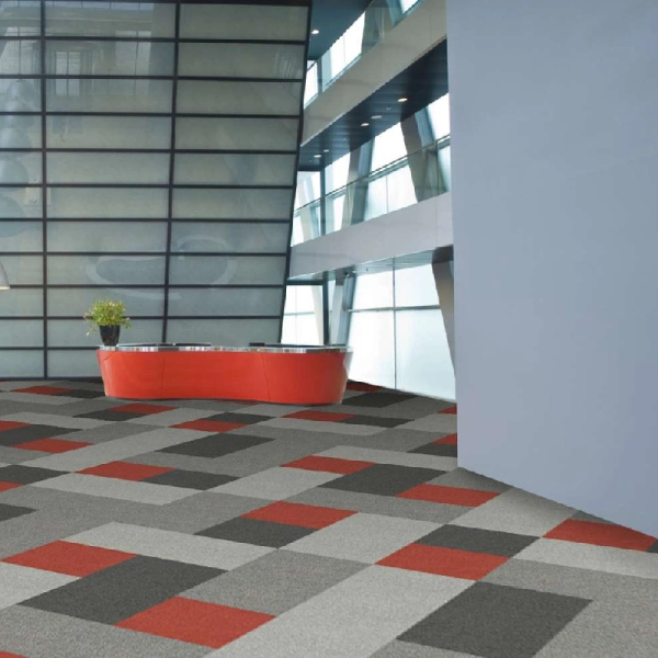 geometric block carpet tiles in grey, charcoal, and red in a lobby.